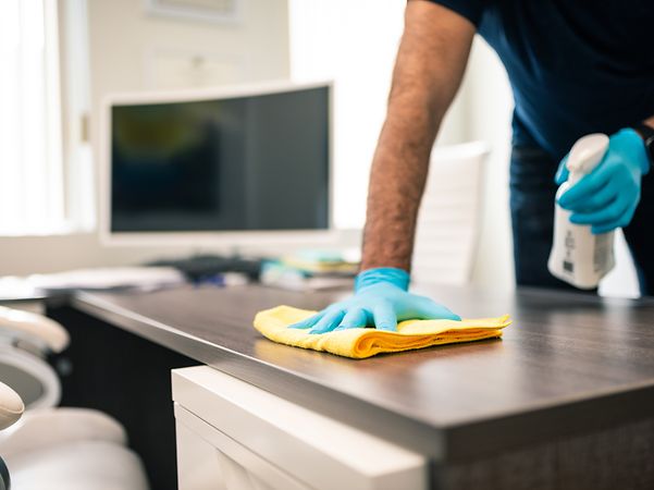 Cleaner wipes desk in office with cleaning cloth.