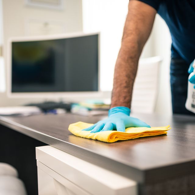 Cleaner wipes desk in office with cleaning cloth.