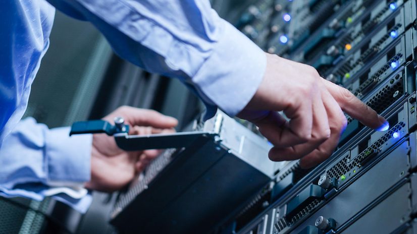 En IT-tekniker arbetar vid ett serverrack i ett datacenter och kontrollerar de upplysta statuslamporna.