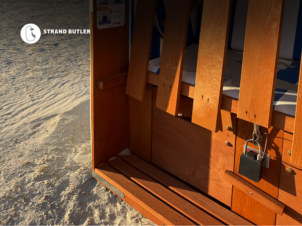 Strandbutlers logotyp framför en strandkorg på sand med havet i bakgrunden