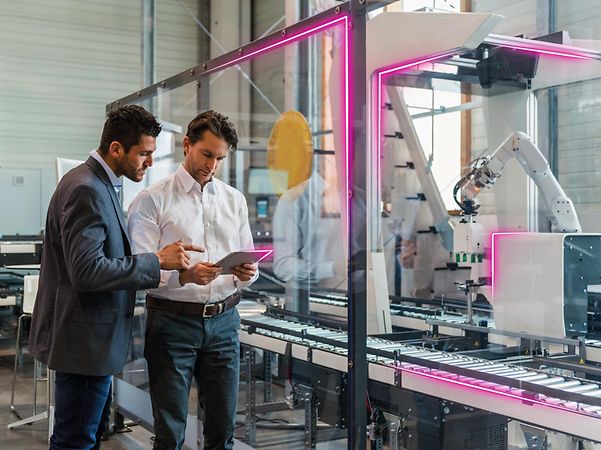 Dos personas trabajando con una tableta para gestionar la conectividad frente a una línea de producción en funcionamiento