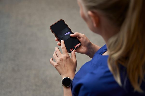 Una mujer con uniforme de enfermera sostiene un teléfono inteligente y escribe con los dedos