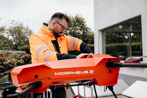 A technician is preparing a Morpheus transport drone for deployment in front of a building.