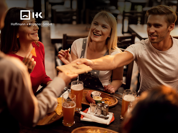 Logo von Hoffmann + Krippner vor einer Gruppe junger Menschen in einem Restaurant