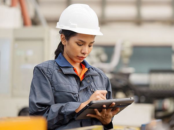 Frau mit Helm in Fabrikhalle schreibt auf ein Tablet