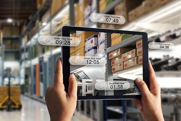 Ein Lager mit Regalen voller Kartons und einem Tablet im Vordergrund, das eine Augmented-Reality-Oberfläche zeigt.
