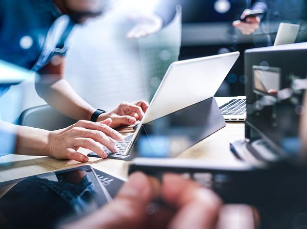 Mensch berührt Laptop und Tablet auf einem Tisch mit abstrakter Netzdarstellung.