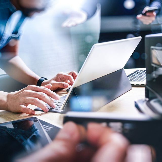 Mensch berührt Laptop und Tablet auf einem Tisch mit abstrakter Netzdarstellung.