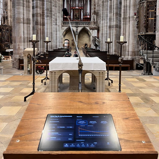 Kirchenraum mit Altar, Mikrofon und digitalem Bedienpanel im Vordergrund.