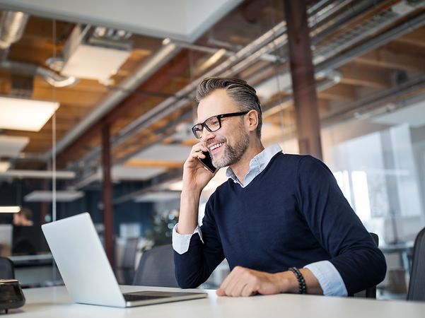 Geschäftsmann telefoniert im Büro und arbeitet am Laptop – digitale Kommunikation vernetzt Arbeit und Mobilität.