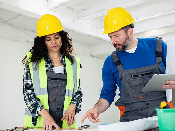 Frau und Mann mit Tablet studieren Baupläne im Rohbau