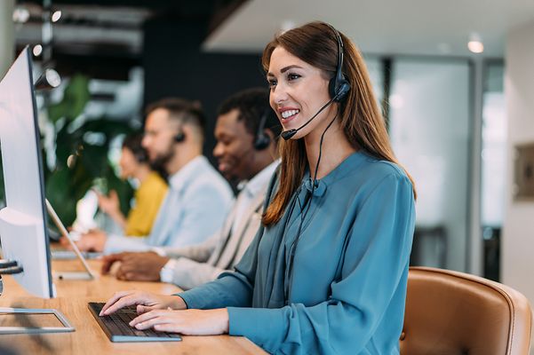 Woman with headset sitting at a desk and smiling.