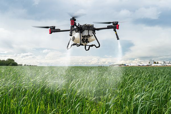 Drone spraying liquid over a green field.
