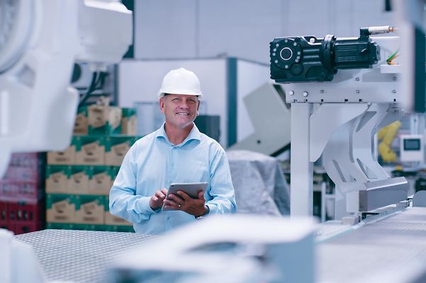 Man wearing safety helmet holding tablet in a production hall.