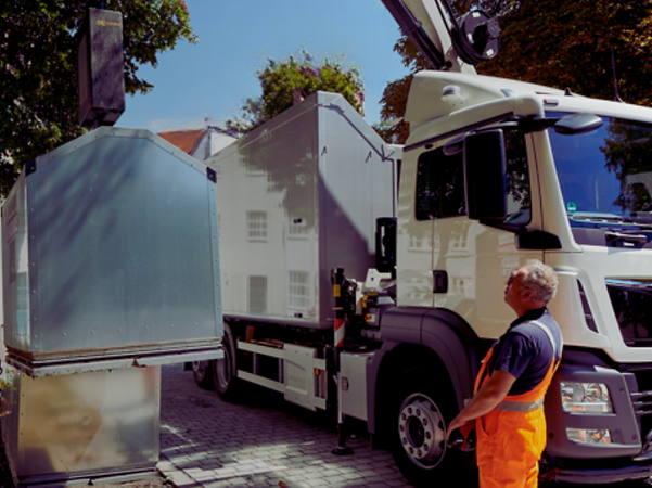 A garbage collector operates the crane of a truck to empty a glass container