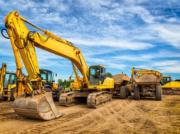 A yellow excavator stands in front of two dump trucks