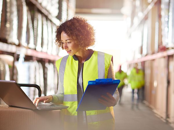 An employee in a high-visibility vest checks data on the laptop